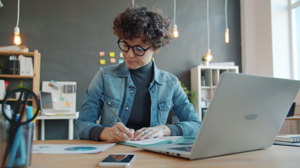 Founder analyzing marketing data and taking notes at a desk with a laptop in a creative office